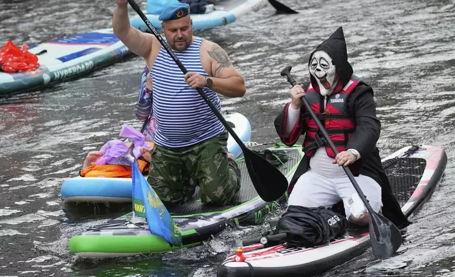 A retired Russian military paratrooper, left, steers his stand-up paddle (SUP) board along the Moyka River at the annual costumed 'Fontanka' SUP-boards festival attracting more than 10,000 participants, in St. Petersburg, Russia, Saturday, Aug. 2, 2025. (AP Photo/Dmitri Lovetsky)