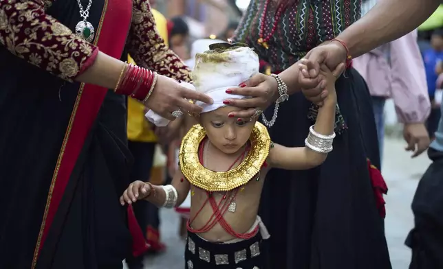 Devotees adjust a lighted oil lamp on the head of a child during a parade celebrating the birthday of Lord Krishna on Krishna Janmashtami festival in Bhaktapur, Nepal, Saturday, Aug. 16, 2025. (AP Photo/Niranjan Shrestha)
