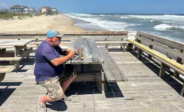 Dave Cowles eats a burrito at Rodanthe Pier as waves from Hurricane Erin crash along beach at Rodanthe, N.C., on Tuesday, Aug. 19, 2025. (AP Photo/Allen G. Breed)