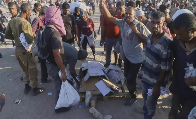 Palestinians stand next the body of a woman who was hit by a truck while attempting to reach a humanitarian aid convoy moving along the Morag corridor near Rafah, in the southern Gaza Strip, Monday, Aug. 4, 2025. (AP Photo/Mariam Dagga)