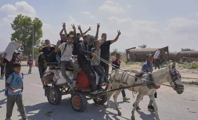 Palestinians wave to the camera as they carry humanitarian aid packages near a Gaza Humanitarian Foundation distribution center operated by the U.S.-backed organization, in Netzarim, central Gaza Strip, Monday, Aug. 4, 2025. (AP Photo/Abdel Kareem Hana)