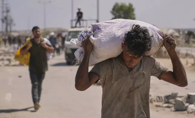 A Palestinian carries a bag containing aid near a Gaza Humanitarian Foundation distribution center operated by the U.S.-backed organization, in Netzarim, central Gaza Strip, Monday, Aug. 4, 2025. (AP Photo/Abdel Kareem Hana)