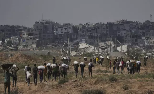 Palestinians carry humanitarian aid packages near a Gaza Humanitarian Foundation distribution center operated by the U.S.-backed organization, in Netzarim, central Gaza Strip, Monday, Aug. 4, 2025. (AP Photo/Abdel Kareem Hana)