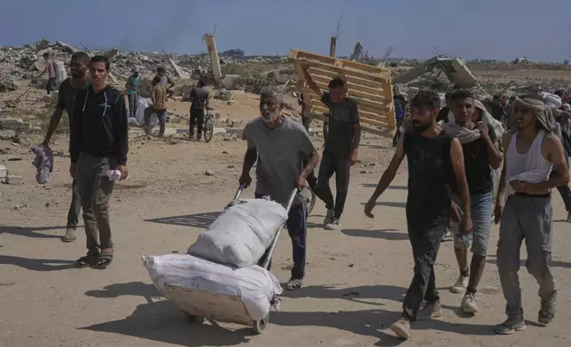 Palestinians carry humanitarian aid packages near a Gaza Humanitarian Foundation distribution center operated by the U.S.-backed organization, in Netzarim, central Gaza Strip, Monday, Aug. 4, 2025. (AP Photo/Abdel Kareem Hana)
