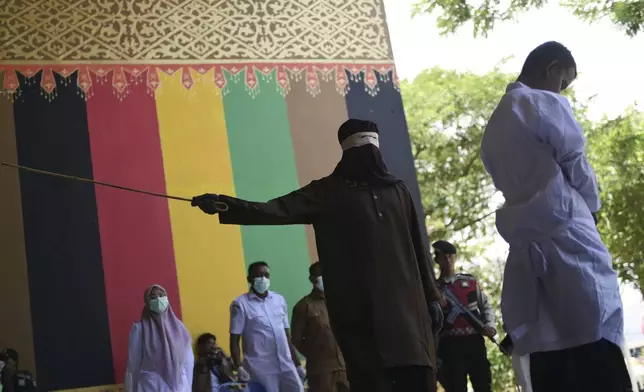 An official uses a rattan cane to whip one of two men convicted of violating Islamic law by hugging and kissing, which the court ruled can lead to banned sexual relations, in Banda Aceh, Aceh province, Indonesia, Tuesday, Aug. 26, 2025. (AP Photo/Reza Saifullah)