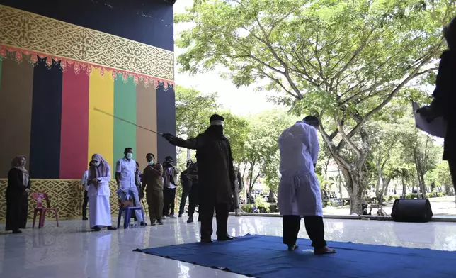 An official uses a rattan cane to whip one of two men convicted of violating Islamic law by hugging and kissing, which the court ruled can lead to banned sexual relations, in Banda Aceh, Aceh province, Indonesia, Tuesday, Aug. 26, 2025. (AP Photo/ Reza Saifullah)