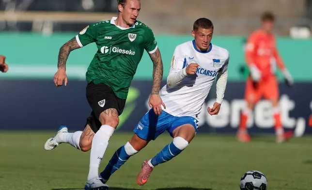 Hertha's Mickael Cuisance, right, and Muenster's Marvin Schulz, left, challenge for the ball during the German soccer cup first round match between Preussen Muenster and Hertha BSC in Muenster, Germany, Monday, Aug. 18, 2025. (Friso Gentsch/dpa via AP)