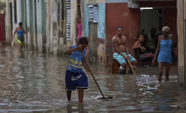 A youth sweeps away trash blocking drains on a flooded street after heavy rains in Havana, Monday, Aug. 11, 2025. (AP Photo/Ramon Espinosa)