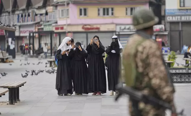 Muslim women take pictures as Indian paramilitary soldiers stand guard while others march holding the Indian flag as part of a campaign encouraging every household to hoist the national flag ahead of the Indian independence anniversary in Srinagar, Indian controlled Kashmir, Tuesday, Aug. 12, 2025. (AP Photo/Mukhtar Khan)