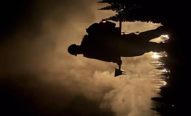 In this photo provided by the Hurricane Valley Fire District, a firefighter is silhouetted by the Monroe Canyon Fire near Monroe, Utah, July 16, 2025. (Hurricane Valley Fire District via AP)