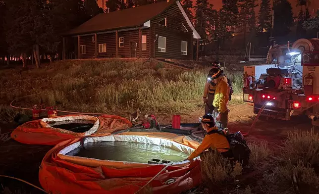 In this photo provided by the Hurricane Valley Fire District, firefighters fill self-supporting tanks while working to subdue the Monroe Canyon Fire near Monroe, Utah, Friday, July 25, 2025. (Hurricane Valley Fire District via AP)