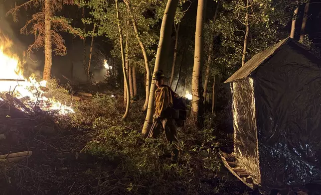 In this photo provided by the Hurricane Valley Fire District, a firefighter stands in front of the Monroe Canyon Fire near Monroe, Utah, Friday, July 25, 2025. (Hurricane Valley Fire District via AP)