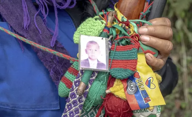 Patricia Elago Zetty, an Indigenous Guard, poses for a photo with her staff and a small photo of her son on it July 16, 2025, in Caldono, Colombia. (AP Photo/Nadège Mazars)