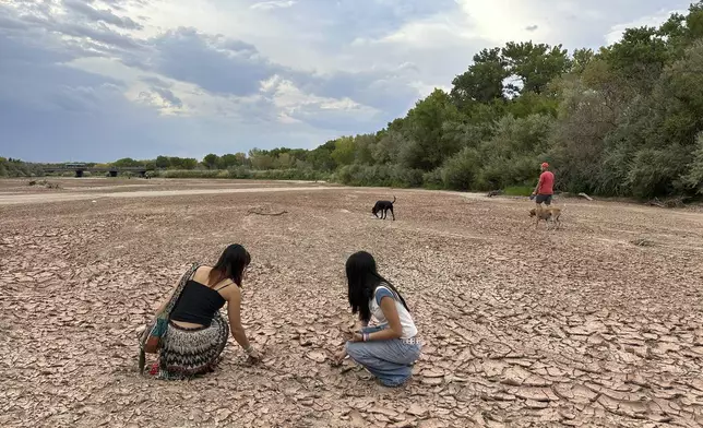 Sisters Zoe Hughes, left, and Phoebe Hughes, center, collect pieces of clay from the Rio Grande as a man walks his dogs in the dry riverbed in Albuquerque, N.M., on Thursday, Aug. 21, 2025. (AP Photo/Susan Montoya Bryan)