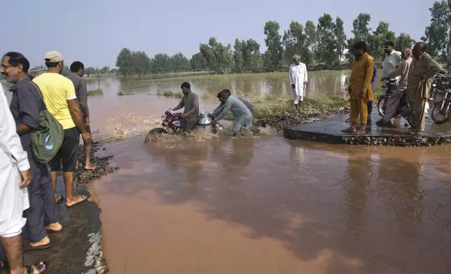 Villagers help a milkman crossing the flooded portion of a road damaged by floods after torrential rains on the outskirts of Sodhra town, in Wazirabad district, Pakistan, Friday, Aug. 29, 2025. (AP Photo/A. Rizvi)