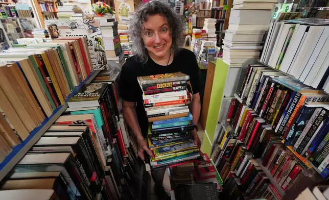 Michelle Souliere, owner of the Green Hand Bookstore, carries a stack of books to the shelves, in Portland, Maine, on Thursday, Aug. 7, 2025. (AP Photo/Robert F. Bukaty)