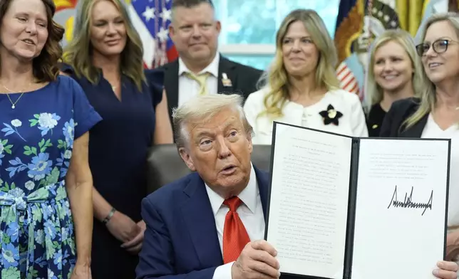 President Donald Trump, surrounded by family members of soldiers killed in Afghanistan at the attack at Abbey Gate, holds up a signed proclamation honoring the fourth anniversary of the attack, in the Oval Office of the White House, Monday, Aug. 25, 2025, in Washington. (AP Photo/Alex Brandon)