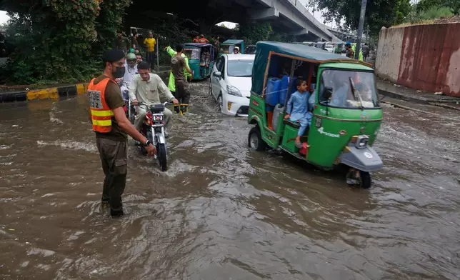 A police officer directs vehicles and motorcyclists driving through a flooded road after heavy rainfall in Peshawar, Pakistan, Monday, Aug. 18, 2025. (AP Photo/Muhammad Sajjad)