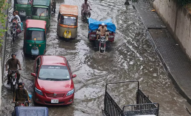 Vehicles and motorcyclists drive through a flooded road after heavy rainfall in Peshawar, Pakistan, Monday, Aug. 18, 2025. (AP Photo/Muhammad Sajjad)