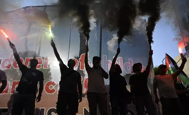 Protesters hold flares during a rally to protest the arrival of a cruise ship with Israelis, in Piraeus port, Greece, Thursday, Aug. 14, 2025. (AP Photo/Michael Varaklas)