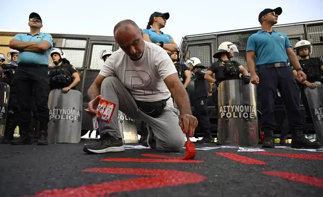 A protester paints a slogan on the ground, in front of police forces, during a rally to protest the arrival of a cruise ship with Israelis, in Piraeus port, Greece, Thursday, Aug. 14, 2025. (AP Photo/Michael Varaklas)