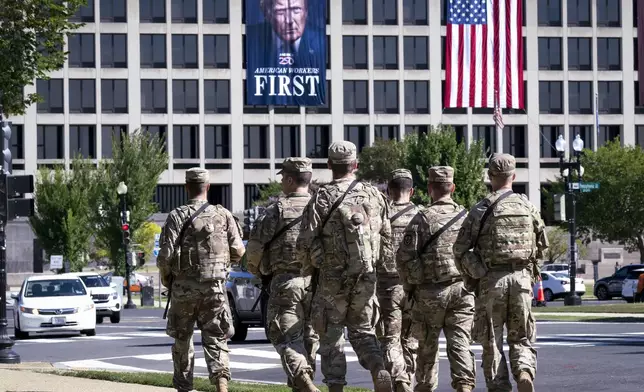 Armed National Guard soldiers from West Virginia patrol the Mall near the Labor Department in Washington, where a poster of President Donald Trump is displayed, Tuesday, Aug. 26, 2025. (AP Photo/J. Scott Applewhite)