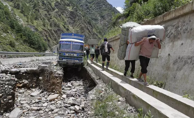 FILE - People carry goods from a damaged truck stuck after monsoon rains swept away a key bridge connecting the country with China in Rasuwagadi, north of the capital, Kathmandu, Nepal, July, 9, 2025. (AP Photo/Sujan Gurung, File)