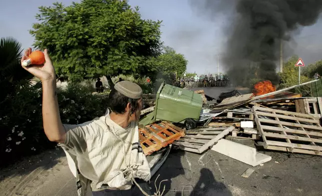 FILE - A Jewish settler prepares to throw a light bulb filled with orange paint at Israeli police, as they arrive in the Jewish settlement of Gadid, Aug. 19, 2005. (AP Photo/David Guttenfelder, File)