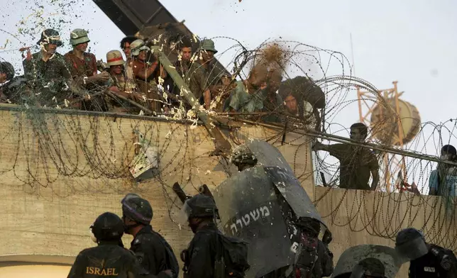 FILE - Israeli police officers storm the rooftop of a synagogue, battling dozens of protesters who threw acid, sand and buckets of green liquid and tried to hit officers with sticks, in the Jewish settlement of Kfar Darom, in the southern Gaza Strip, Aug. 18, 2005. (AP Photo/Lefteris Pitarakis)