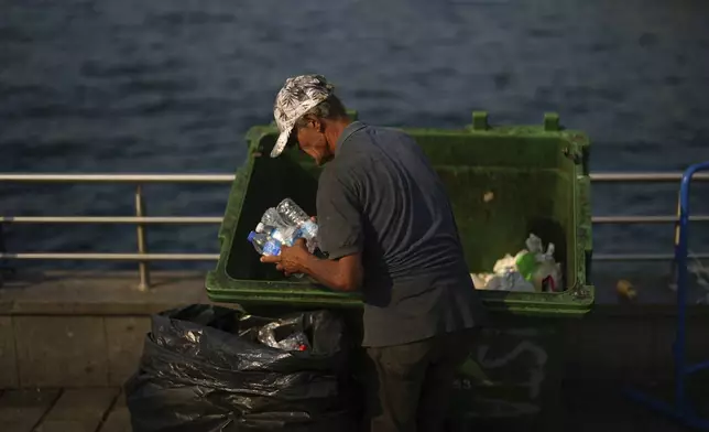 A garbage collector takes discarded plastic bottles from a street trash bin at Eminonu, in Istanbul, Turkey, Friday, Aug. 8, 2025. (AP Photo/Francisco Seco)