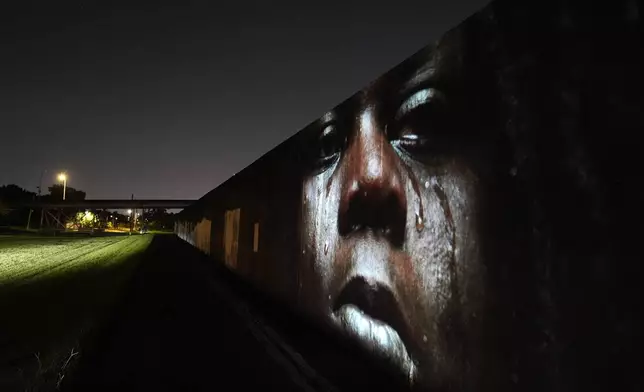 This photo of Leonard Thomas, 23, crying in the aftermath of Hurricane Katrina in New Orleans, taken by AP photographer Rick Bowmer, is projected Wednesday, Aug. 13, 2025, onto the flood wall in the Lower Ninth Ward, which was breached, flooding major parts of the city. (AP Photo/Gerald Herbert)