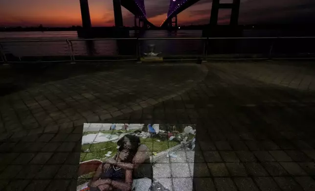 This photo showing flood victims sitting at the Ernest N. Morial Convention Center where they had been waiting for days to be evacuated in the aftermath of Hurricane Katrina in New Orleans, taken by AP photographer Eric Gay, is projected Tuesday, Aug. 26, 2025, along the Mississippi River behind the convention center. (AP Photo/Gerald Herbert)