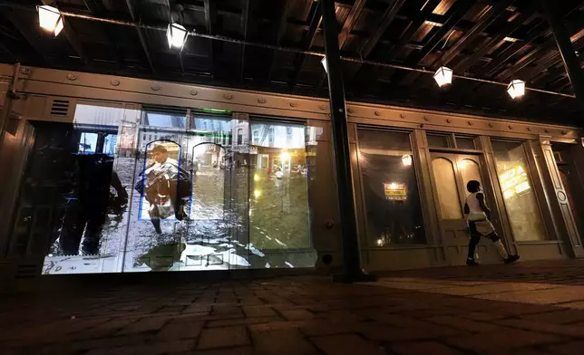 This photo of people taking goods from stores on Canal Street in downtown New Orleans in the aftermath of Hurricane Katrina, taken by AP photographer Eric Gay, is projected Wednesday, Aug. 20, 2025, onto a storefront in the same location. (AP Photo/Gerald Herbert)