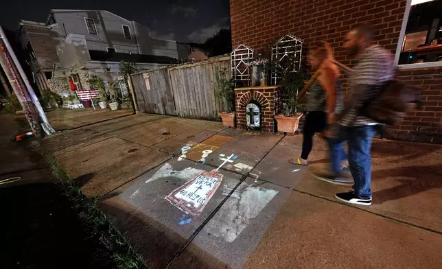 This photo of a makeshift tomb at a New Orleans street corner, concealing a body that had been lying on the sidewalk for days in the wake of Hurricane Katrina, taken by AP photographer Dave Martin, is projected onto the same sidewalk Tuesday, Aug. 19, 2025, in New Orleans. (AP Photo/Gerald Herbert)
