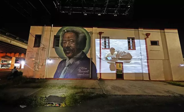 This photo of a young man wading through chest-deep floodwaters in the aftermath of Hurricane Katrina in New Orleans, taken by AP photographer Dave Martin, is projected Monday, Aug. 25, 2025, next to a mural of New Orleans music legend Allen Toussaint, below the overpass where the original photo was made. (AP Photo/Gerald Herbert)