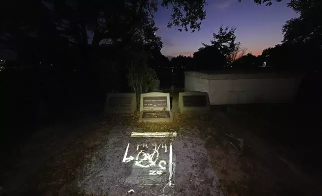 This photo of the FEMA markings indicating a deceased victim in the home of Michael Harrison, who died inside during Hurricane Katrina in Bay St. Louis, Miss., taken by AP photographer Gerald Herbert, nephew of Harrison, is projected Tuesday, Aug. 26, 2025, onto his grave in Pass Christian, Miss. (AP Photo/Gerald Herbert)