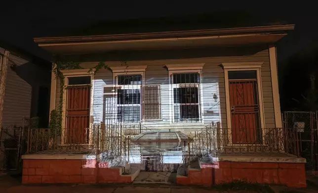 This photo of receding floodwaters leaving their mark on a house and automobile on Orleans Avenue in the aftermath of Hurricane Katrina in New Orleans, taken by AP photographer Ric Francis, is projected Wednesday, Aug. 20, 2025, onto the same house. (AP Photo/Gerald Herbert)