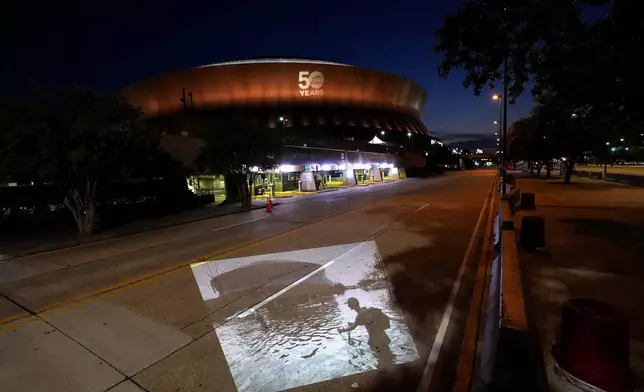 This photo of a man pushing his bicycle through floodwaters near the Superdome in the aftermath of Hurricane Katrina, taken by AP photographer Eric Gay, is projected Wednesday, Aug. 20, 2025, onto the same spot in New Orleans. (AP Photo/Gerald Herbert)