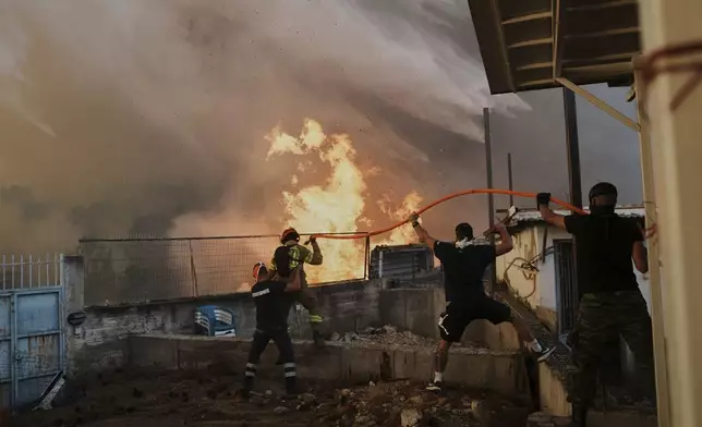 FILE - A firefighter and men try to control the flames approaching a house during a wildfire in Patras city, western Greece, Aug. 13, 2025. (AP Photo/Thanassis Stavrakis, File)