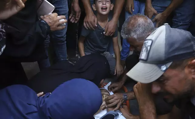 Palestinian relatives mourn over the body of 13-year-old Karim Qdeih, who was killed along with others in overnight Israeli strikes, during his funeral outside Nasser Hospital in Khan Younis, southern Gaza Strip, Saturday, Aug. 23, 2025. (AP Photo/Mariam Dagga)