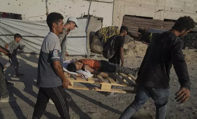 Palestinians carry the body of a boy who was killed while trying to reach a humanitarian aid convoy on the outskirts of Beit Lahiya, as they walk on a road in Gaza City, in the Gaza Strip, Sunday, Aug. 24, 2025. (AP Photo/Abdel Kareem Hana)