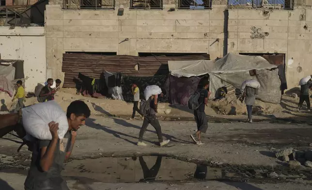 Palestinians carry sacks of flour unloaded from a humanitarian aid convoy that reached Gaza City from the northern Gaza Strip, Sunday, Aug. 24, 2025. (AP Photo/Abdel Kareem Hana)