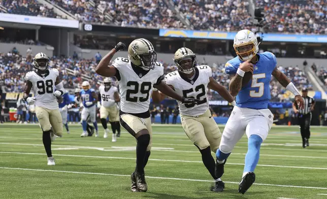 Los Angeles Chargers quarterback Trey Lance (5) runs for a first down past New Orleans Saints linebacker D'Marco Jackson (52) and cornerback Quincy Riley (29) during the first half of a preseason NFL football game Sunday, Aug. 10, 2025, in Inglewood, Calif. (AP Photo/Eric Thayer)