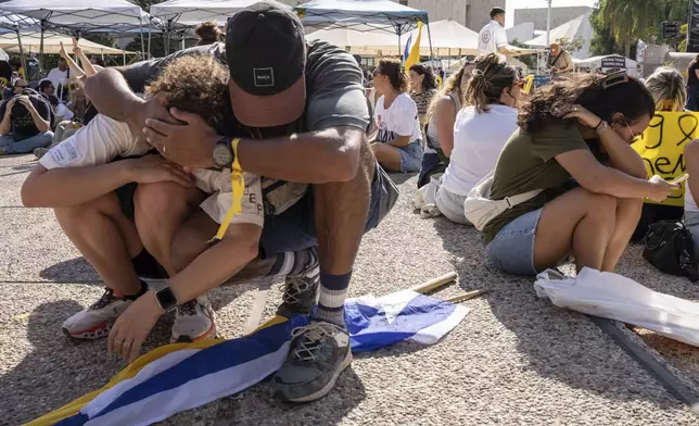 People sit on the ground and cover their heads as a siren sounds a warning of incoming missile fired from Yemen during a protest demanding the immediate release of hostages held by Hamas and calling for the Israeli government to reverse its decision to take over Gaza City and other areas in the Gaza Strip, in Tel Aviv, Israel, Sunday, Aug. 17, 2025. (AP Photo/Maya Levin)