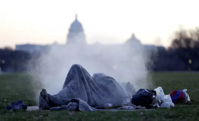 FILE - The U.S. Capitol building gives backdrop to a homeless man resting on a steam vent on the National Mall, Dec. 18, 2019, on Capitol Hill in Washington. (AP Photo/Julio Cortez, File)