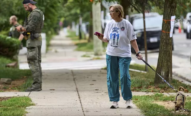 A woman walking her dog watches as officers from several federal agencies including FBI, Federal Marshalls, HSI, and Park Police, arrest a man at an apartment complex, Tuesday, Aug. 19, 2025, in the Petworth neighborhood of northwest Washington. (AP Photo/Jacquelyn Martin)