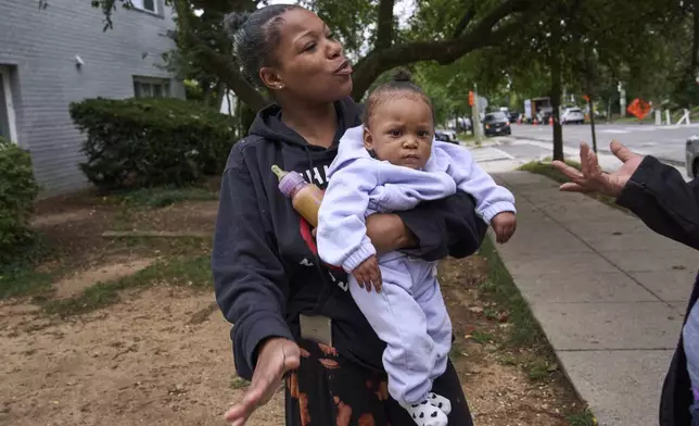 Yanna Stelle, 19, holds her baby Zyanna, 1, as she talks with neighbors in reaction to a large police presence of officers from several federal agencies including Federal Marshalls, Park Police, HSI, and FBI, who arrested a man from within her apartment complex, Tuesday, Aug. 19, 2025, in the Petworth neighborhood of northwest Washington. "That was too many police first thing in the morning," says Stelle, "especially for them just to be doing a warrant. I heard a bunch of walkie talkies and at least 20 officers in the hallways." (AP Photo/Jacquelyn Martin)