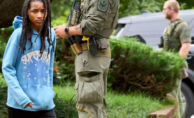 A young person walks out of their apartment building next to armed Park Police as officers from several federal agencies including Federal Marshalls, Park Police, and FBI, arrest a man from within an apartment complex, Tuesday, August 19, 2025, in the Petworth neighborhood of northwest Washington. (AP Photo/Jacquelyn Martin)