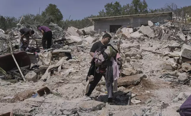 A Palestinian youth carries clothes as he walks over the rubble of a house demolished by the Israeli army in the West Bank village of Beit Sira, near Ramallah, Tuesday, Aug. 19, 2025. (AP Photo/Mahmoud Illean)