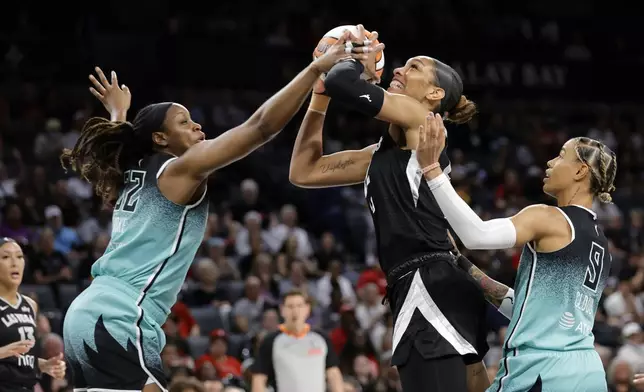 Las Vegas Aces center A'ja Wilson (22) is fouled as she shoots between New York Liberty forward Kennedy Burke (22) and guard Natasha Cloud (9) during the first half of an WNBA basketball game Wednesday, Aug. 13, 2025, in Las Vegas. (Steve Marcus/Las Vegas Sun via AP)